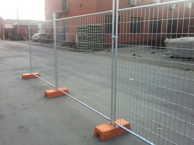 Three galvanized welded temporary fencing on the ground. They are connected by clamps and orange plastic moulded feet.