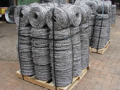 Many coils of barbed wire packaged with the wooden pallets on the ground.