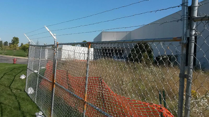 Barbed wire is fixed on the chain link temporary fence and an orange warning barrier fence is fastened on the fence.