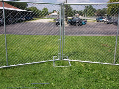 A part of chain link temporary fencing which is installed on lawn. Many cars parked on the ground that next to the lawn.
