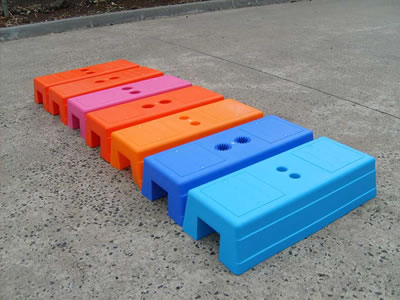 Seven injection moulded temporary fence feet on concrete. Their colors are light blue, dark blue, orange and purple.