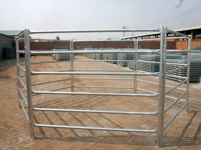 A corral fence stands on the ground of factory. The fence panels with round <d>frame</d> and six round horizontal tubes.
