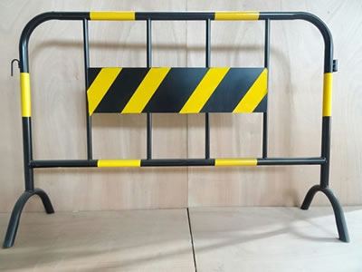 A black and yellow road safety barrier stands on the floor, a metal board are welded at the infilled pipes.