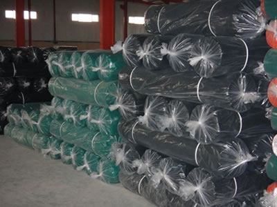 Many green and black shade cloth rolls on the ground, they all packaged with plastic film.