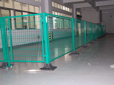 Green powder coated welded temporary fence with a sliding gate is erected in a room. The plastic base is black.