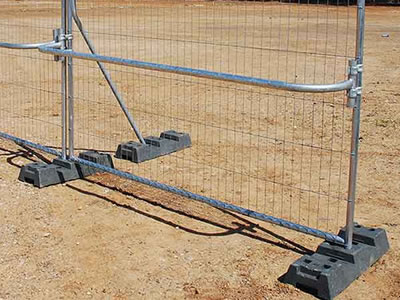 Welded temporary fence is supported by black rubber feet and brace. A handrail installs at the middle of fence.