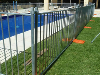 Galvanized temporary pool fence is installed around a swimming pool with orange plastic moulded feet supported.