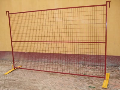 A red Canada temporary fence on the ground. It has a horizontal reinforced pipe at the middle of the mesh.
