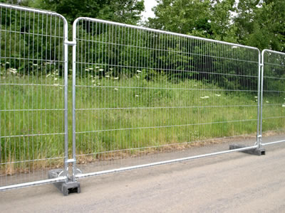 A galvanized temporary fence at roadside. The fence with gray rubber feet has round top.